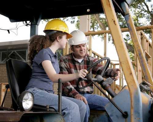 Young girl being taught how to use construction equipment.