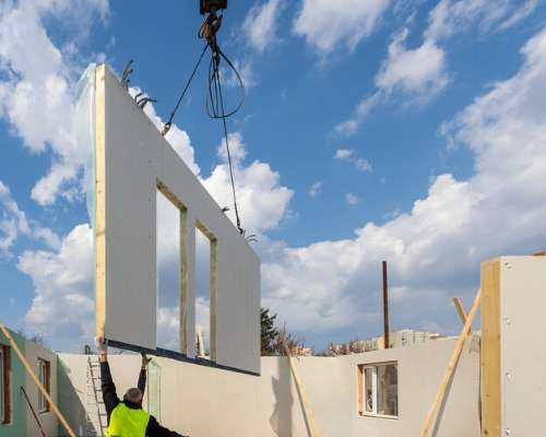 Construction worker guiding a house wall as it is being lowered to the ground by a crane.