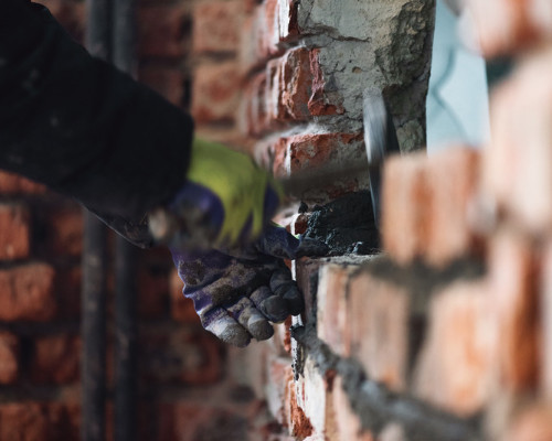 Male bricklayer adding cement onto brickwork